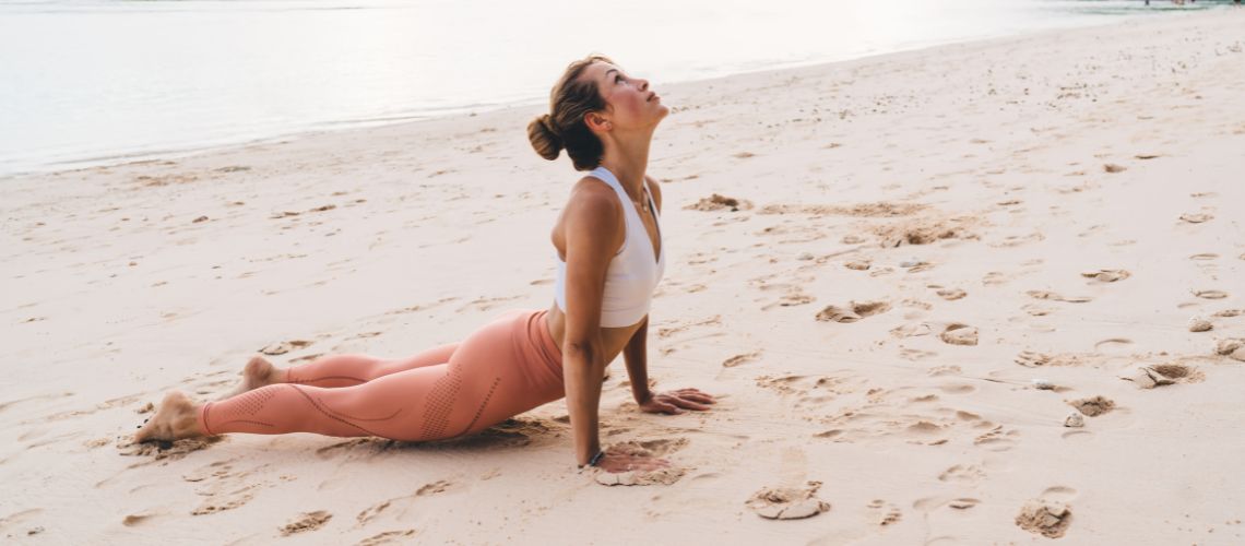 Mujer realizando la postura de la cobra en la playa. 
